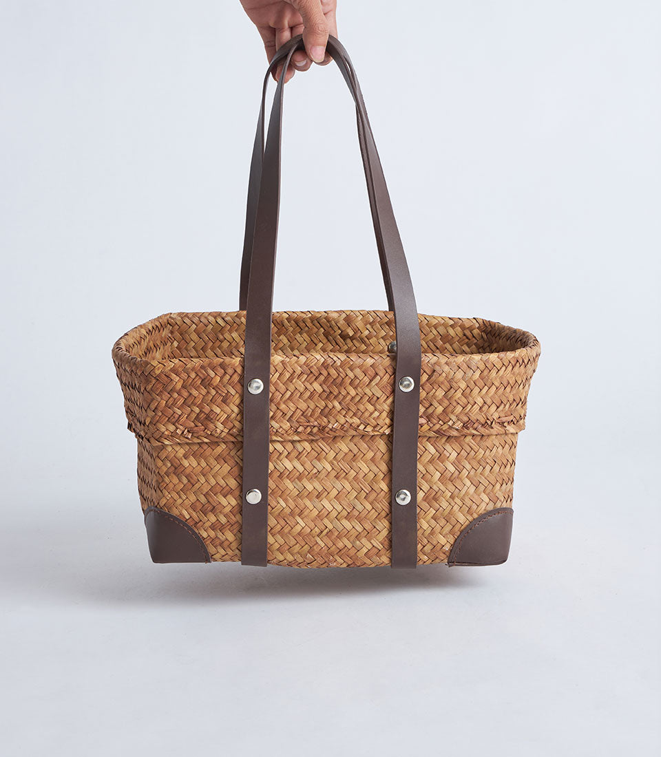 Natural woven straw basket with leather handles and rivets, ideal for luxury gift hampers