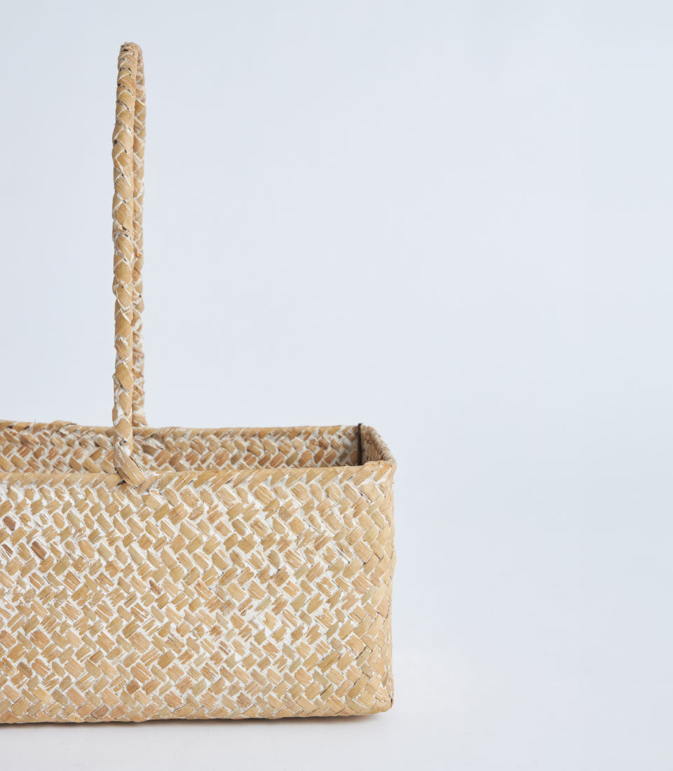 Light natural woven rectangular basket with braided handle, handcrafted from rattan with whitewashed diagonal weave pattern