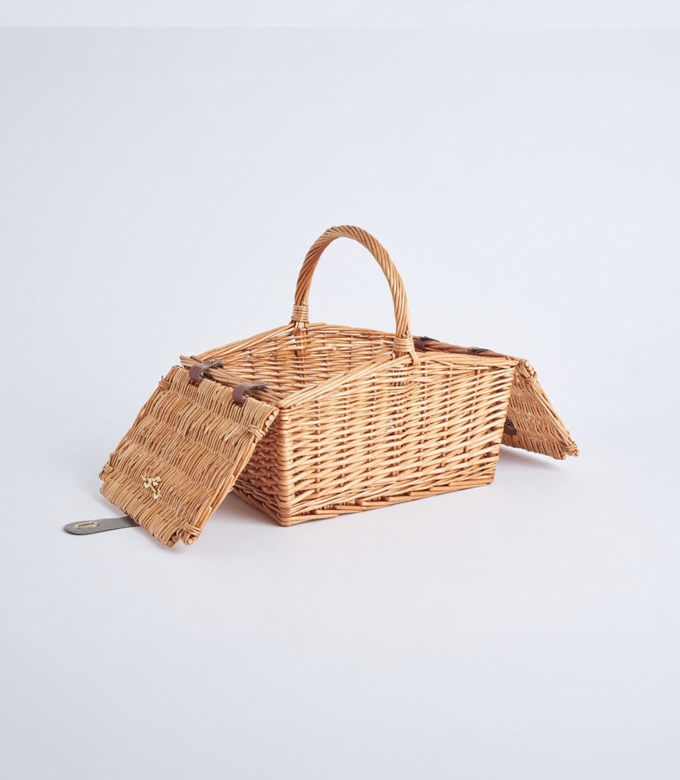 Light brown handwoven wicker picnic basket with leather straps and gold clasp, open lid displayed