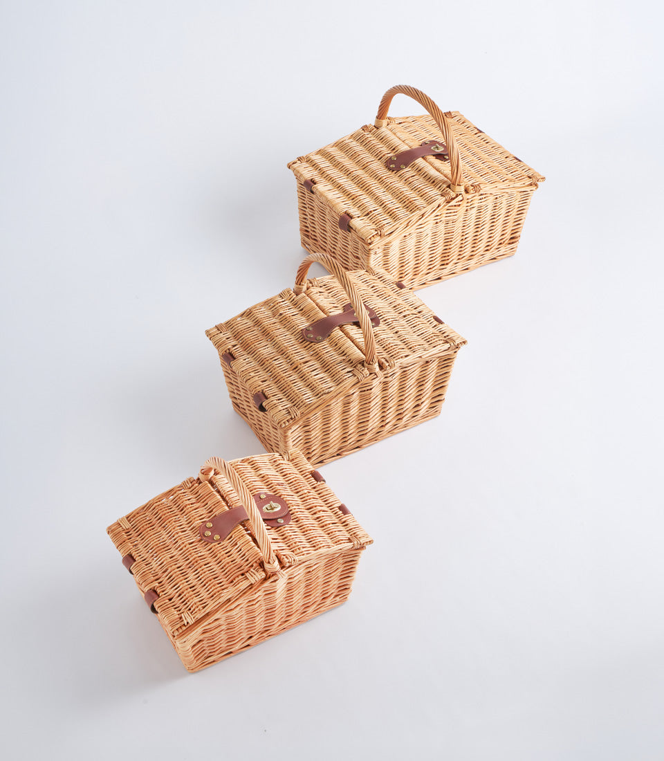 Light brown woven wicker picnic baskets with curved handles, leather straps, and brass buckles for elegant gifting