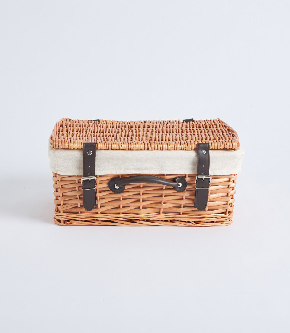 Handwoven light brown wicker picnic basket with cream linen interior and dark leather straps