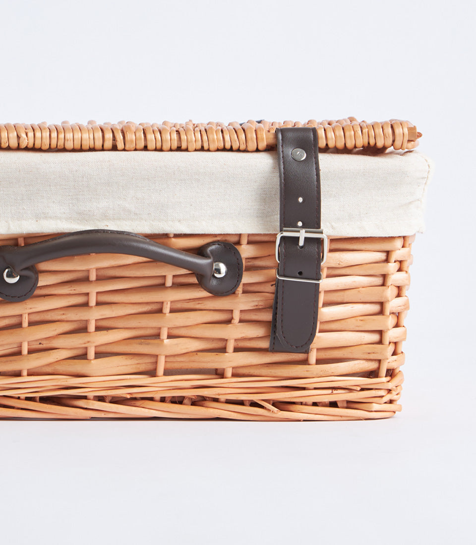 Light brown handwoven wicker picnic basket with leather straps and silver buckle closure