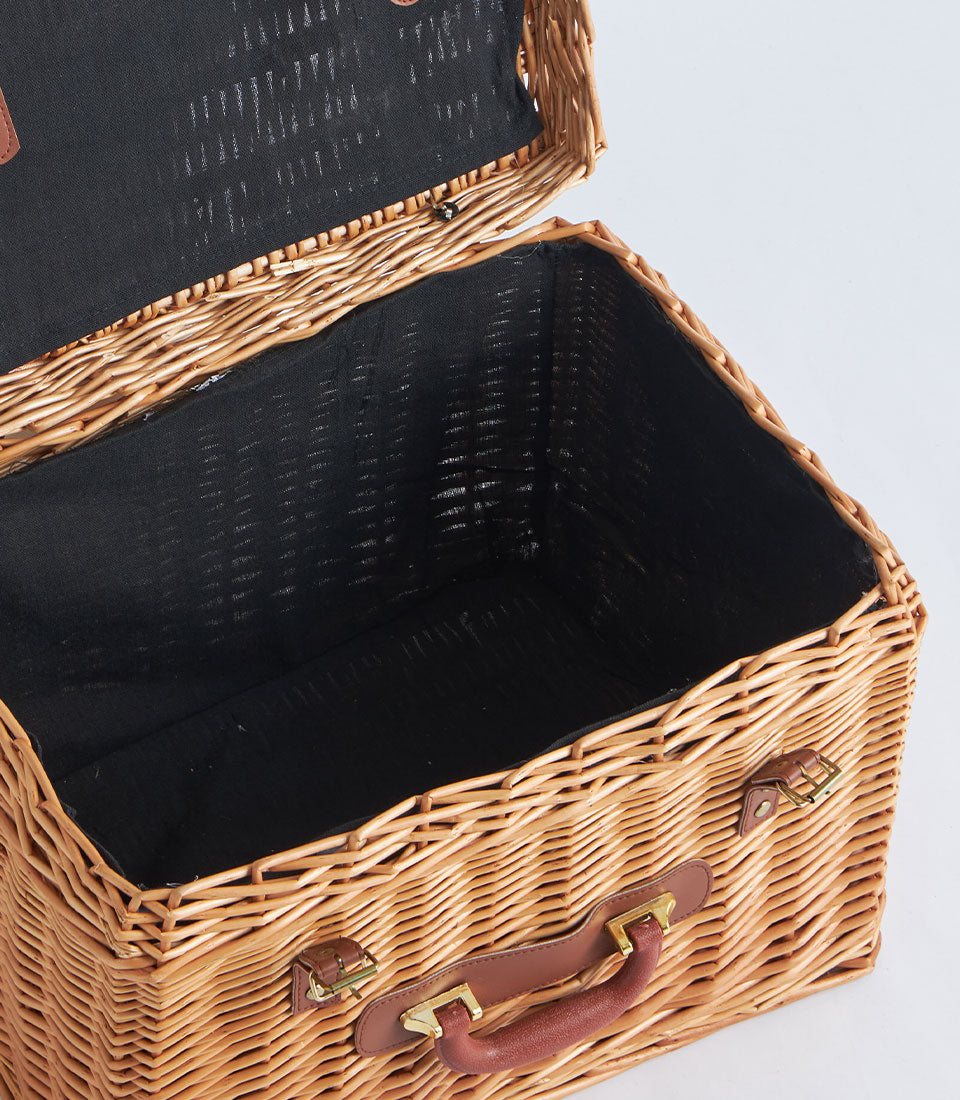Light brown wicker suitcase basket with black fabric lining and leather handles, open view