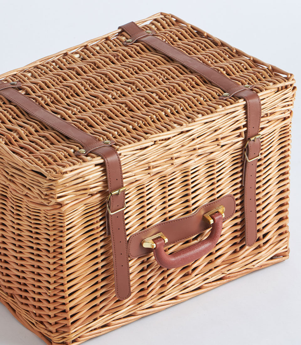Light brown wicker suitcase basket with dark leather straps and gold buckles