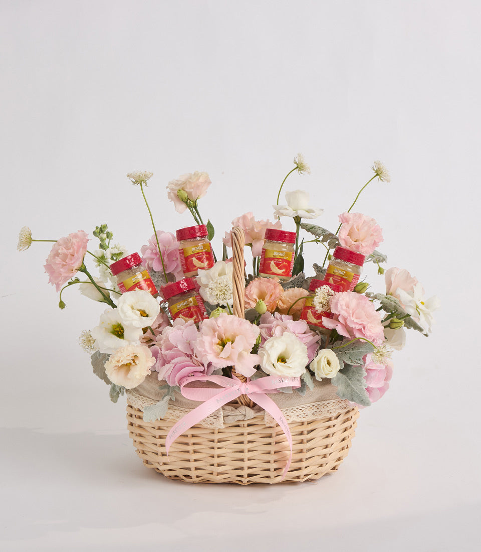 Wicker basket filled with pink and white carnations, queen anne's lace, and red honey jars, tied with pink ribbon.