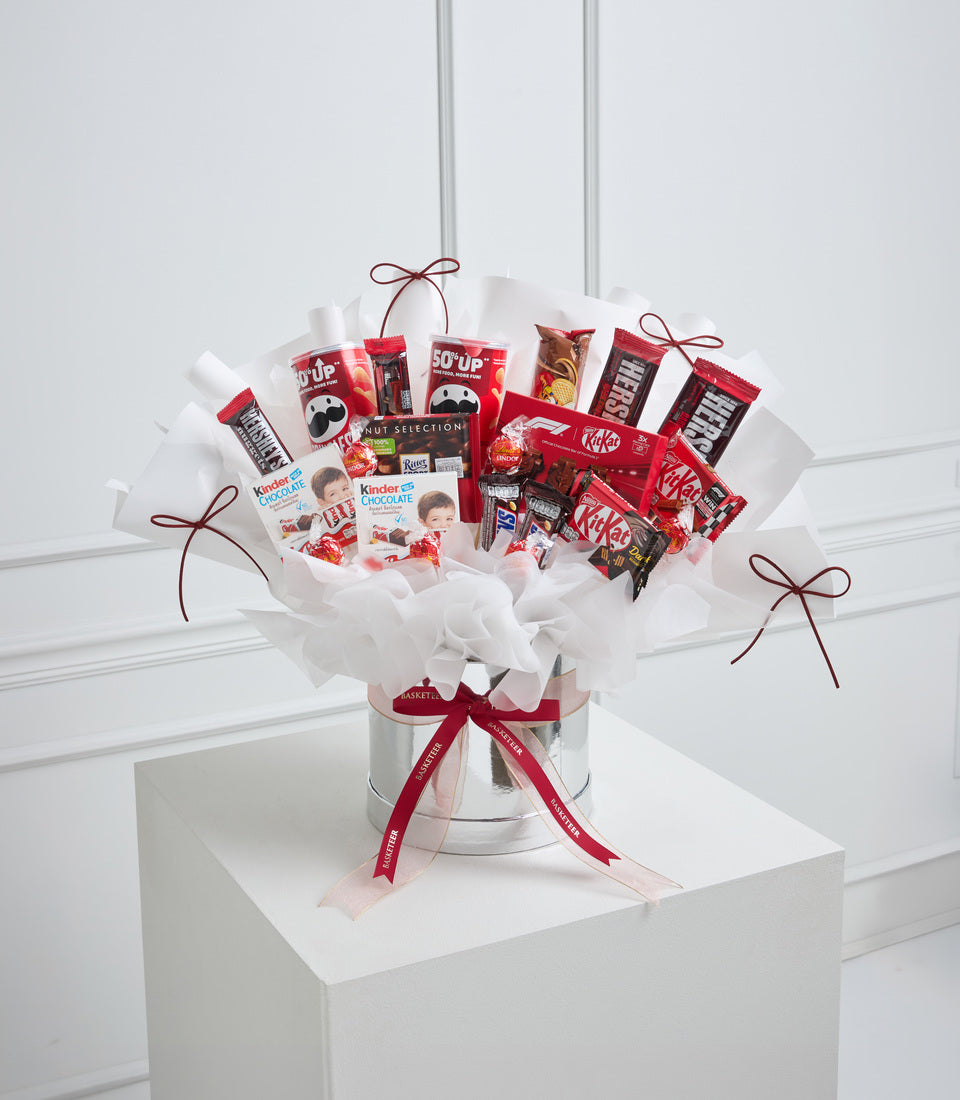 Red and white chocolate gift bouquet in clear vase with white tissue paper, featuring KitKat, Kinder, and Hershey's products tied with burgundy ribbons.