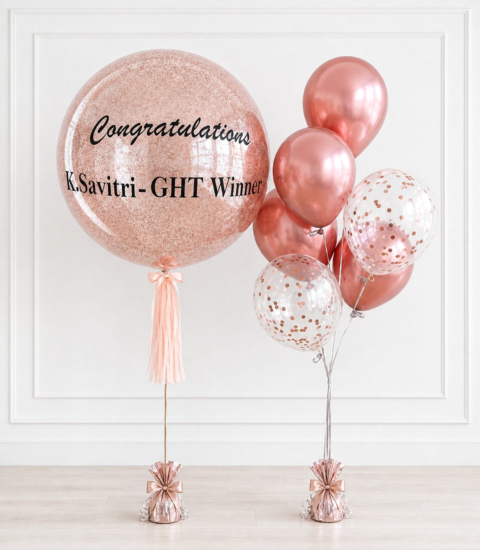 Rose gold glitter balloon with "Congratulations k.Savitri-GHT Winner" text, paired with metallic pink and confetti balloons with tassel weights.