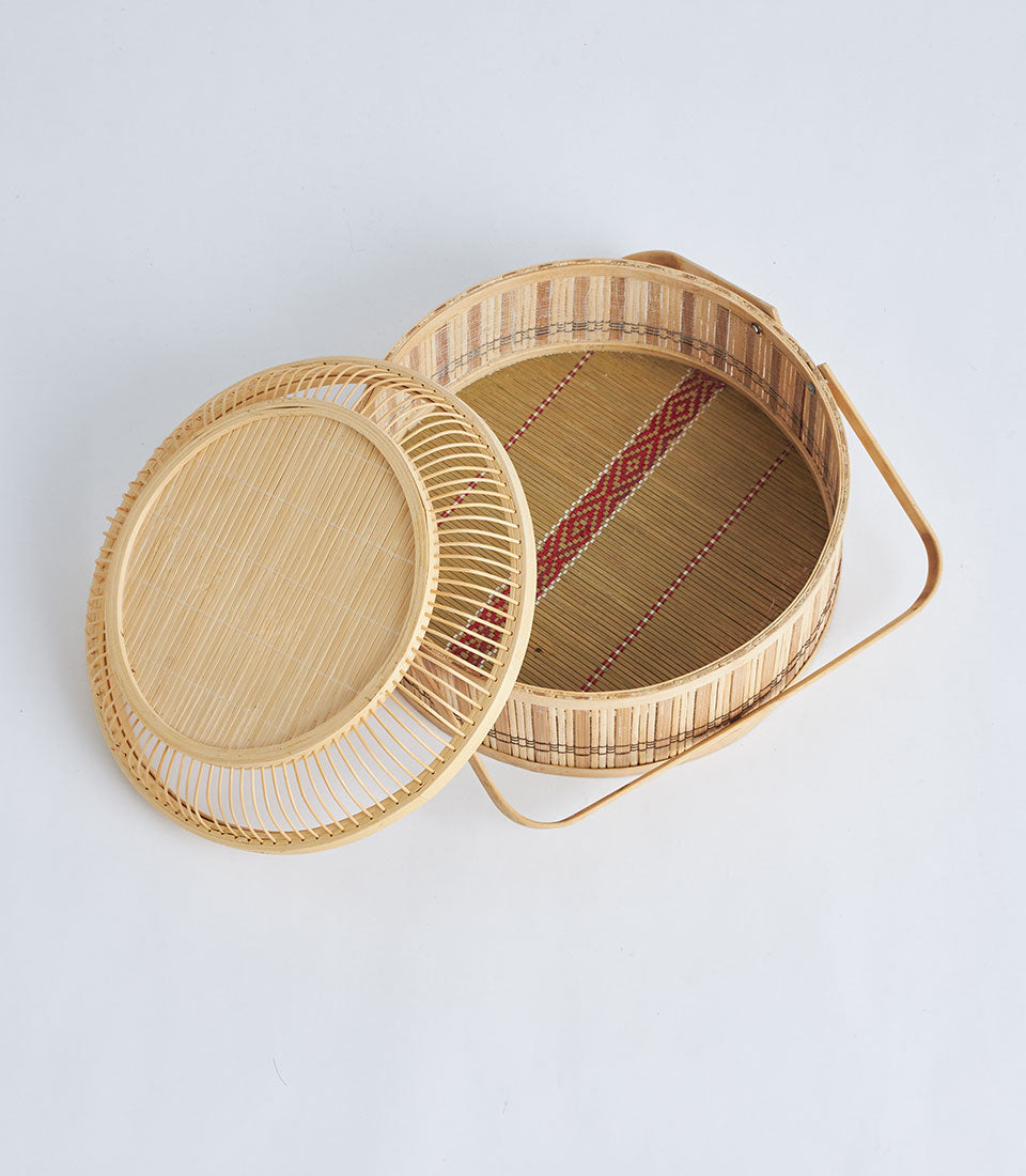 Natural bamboo round basket with woven lid, curved handle, and red geometric linen interior