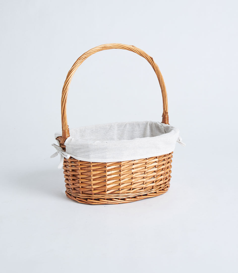 Light brown woven wicker oval basket with fabric liner and arched handle for gift hampers