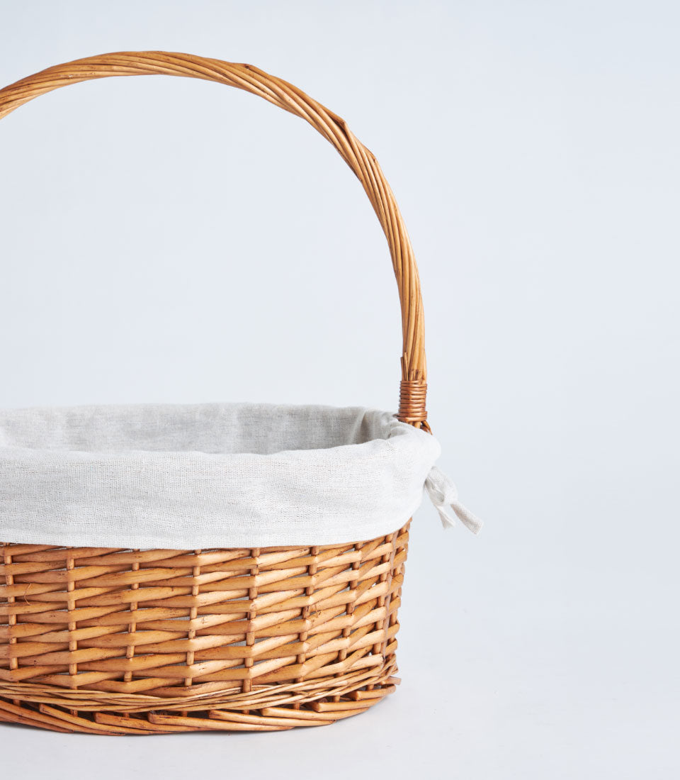 Light brown handwoven wicker basket with arched handle and natural linen fabric liner