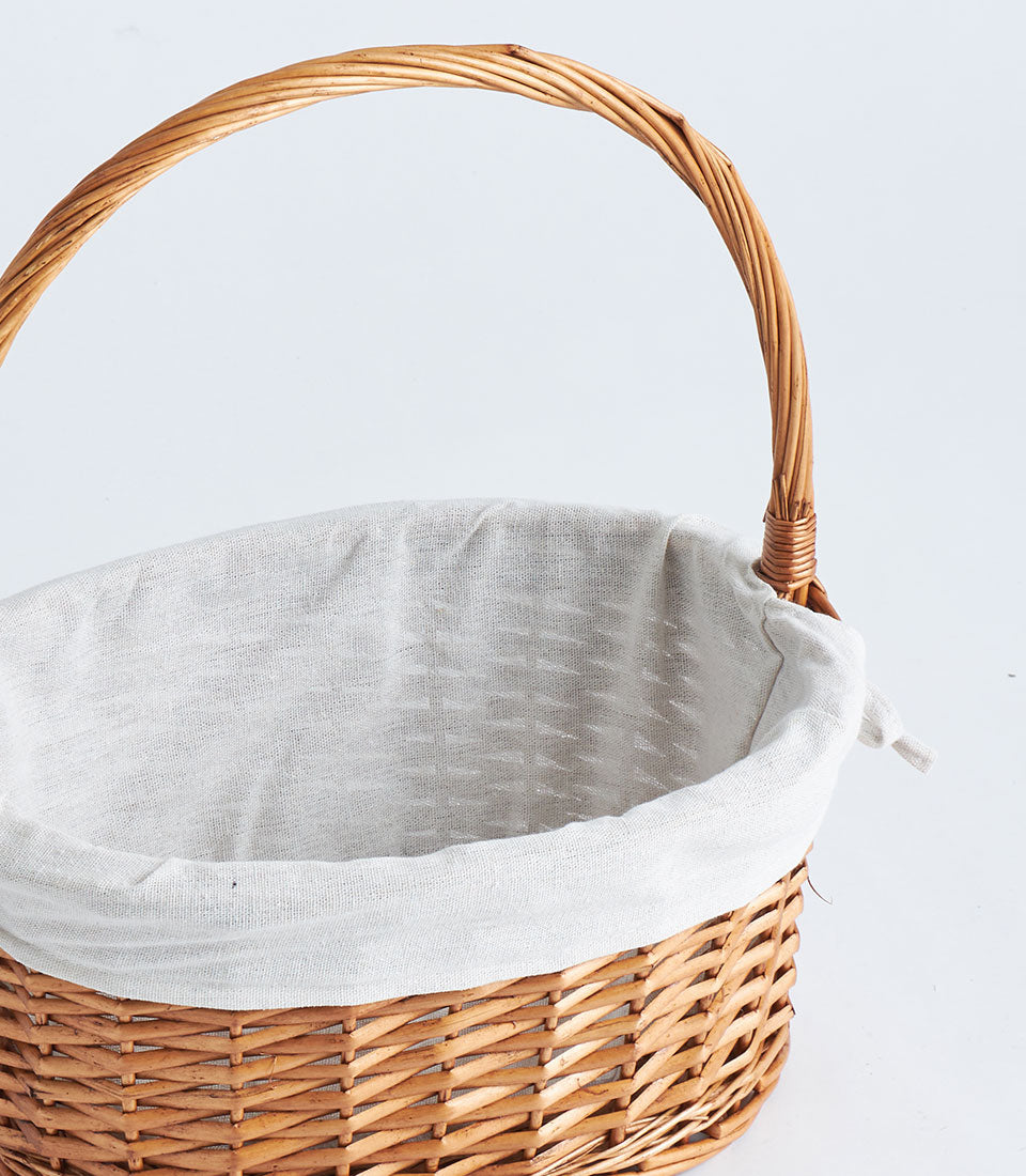 Light brown handwoven oval wicker basket with fabric liner and arched handle