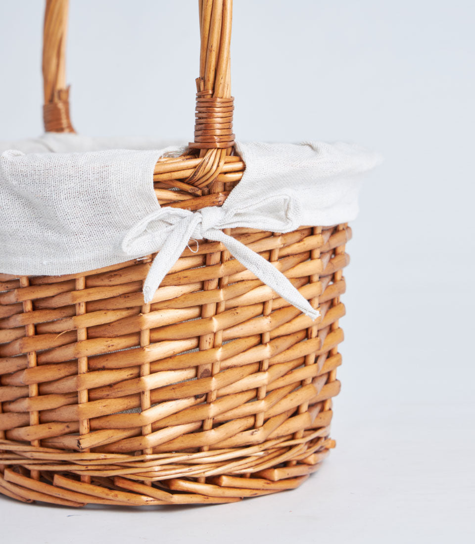 Light brown handwoven wicker basket with white fabric liner and reinforced handle