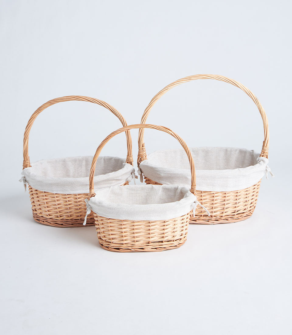 Set of three nested oval wicker gift baskets with linen liners and arched handles in light brown rattan