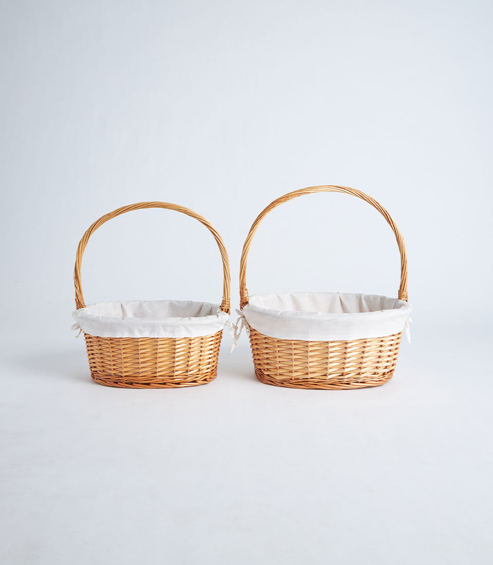 Light brown wicker oval baskets with removable fabric liners and handles, perfect for luxury gift hampers