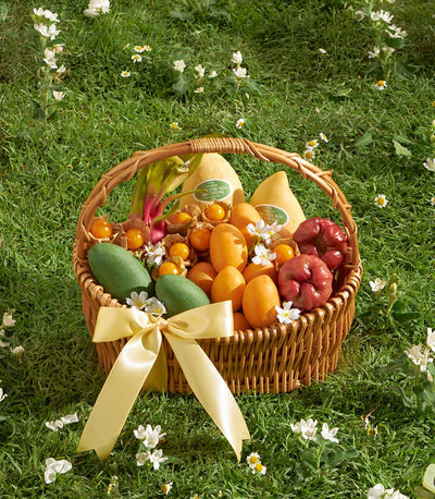 Wicker basket overflowing with tropical mangoes, physalis, and rose apples tied with yellow satin ribbon