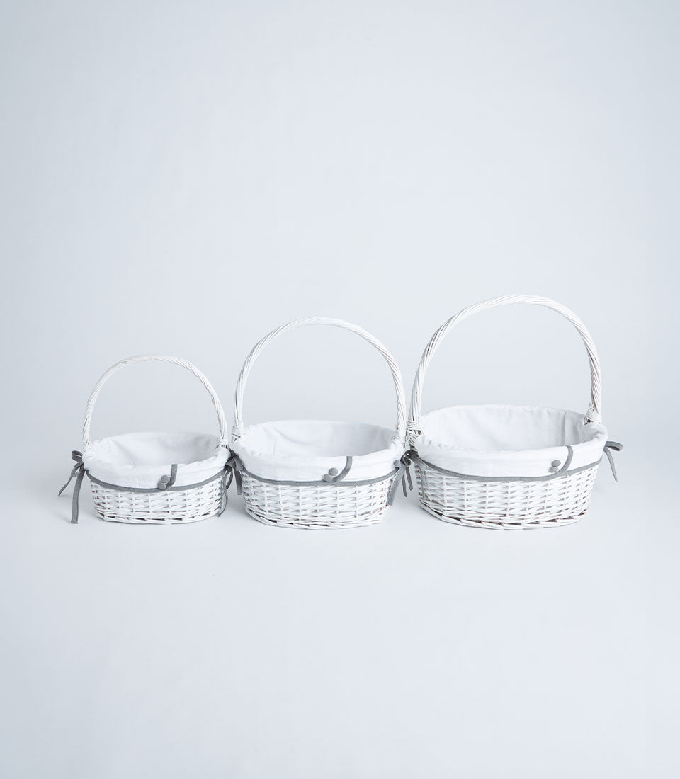 Three white handwoven wicker baskets with grey ribbon trim and fabric liners in graduated sizes