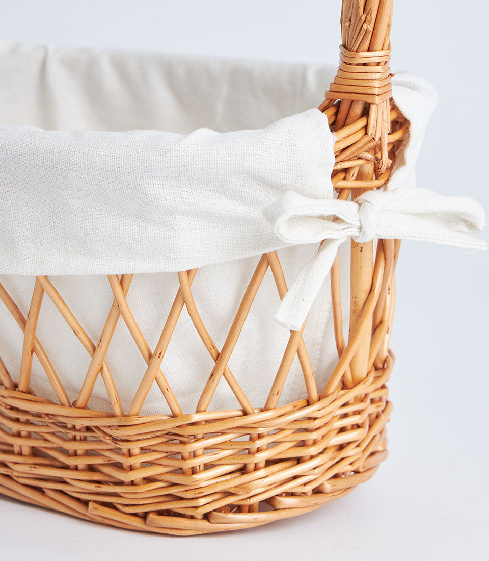 Natural wicker oval gift basket with white fabric lining and gathered bow detail