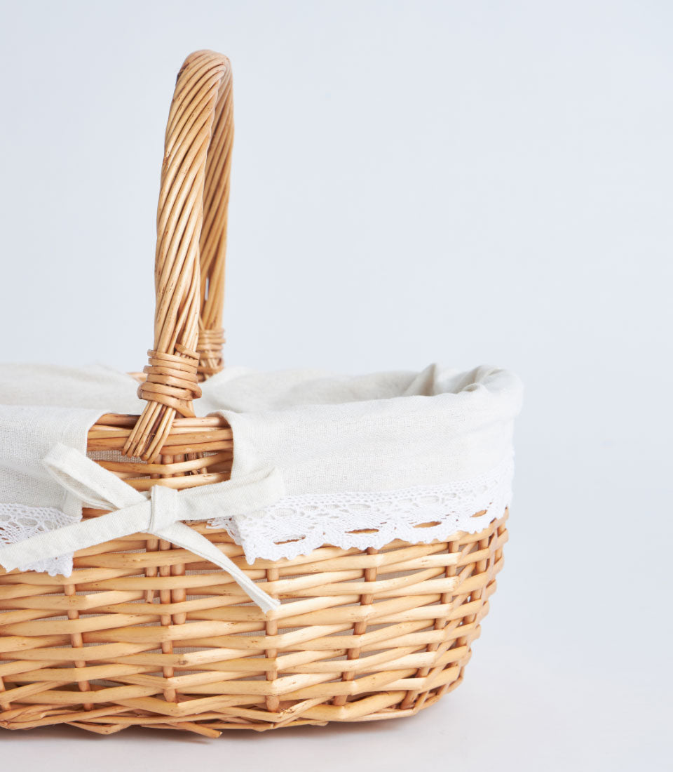Light brown handwoven wicker basket with twisted handle and white lace-trimmed fabric liner