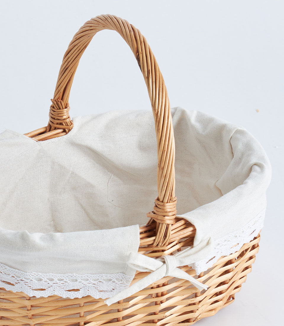Light brown handwoven oval wicker basket with cream lace-trimmed fabric liner and arched handle