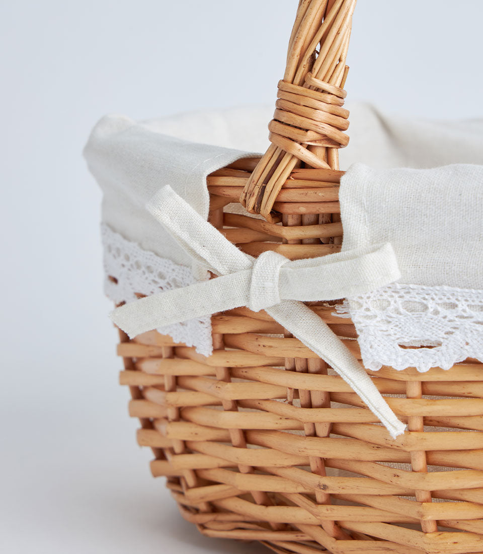 Handwoven light brown wicker gift basket with cream lace liner and white ribbon bow