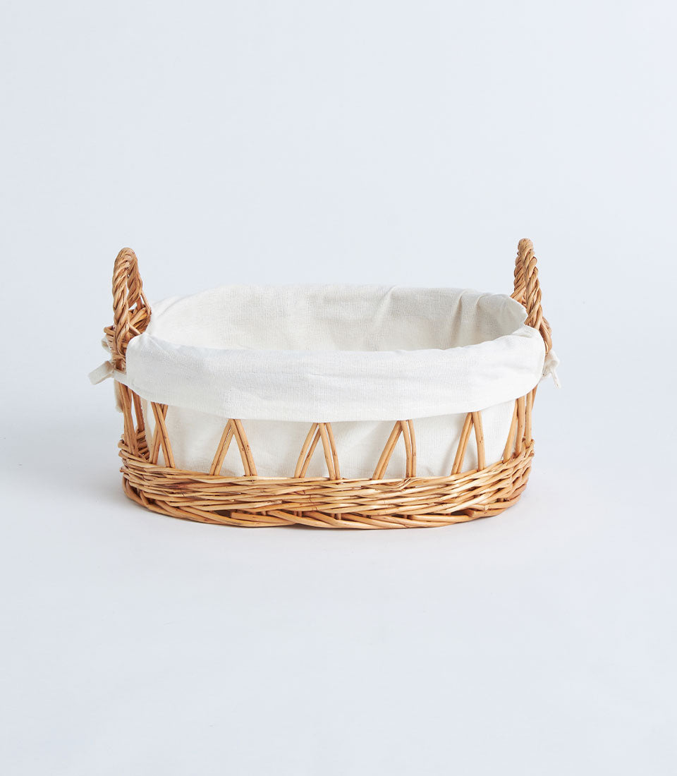 Natural wicker oval basket with white linen lining and braided handles for artisan gift hampers