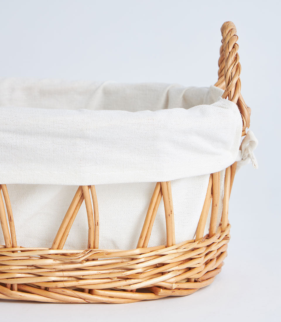 Light brown wicker basket with white linen lining and braided handles for luxury gift hampers