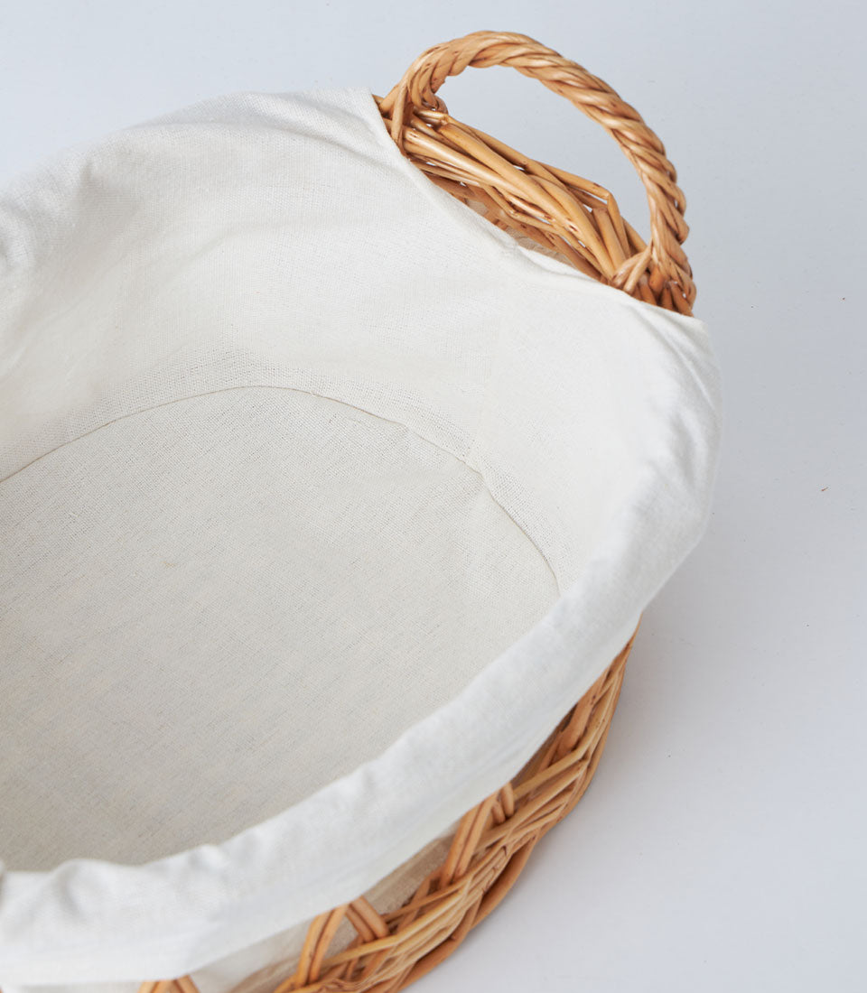 Light brown wicker basket with white linen lining and braided handle