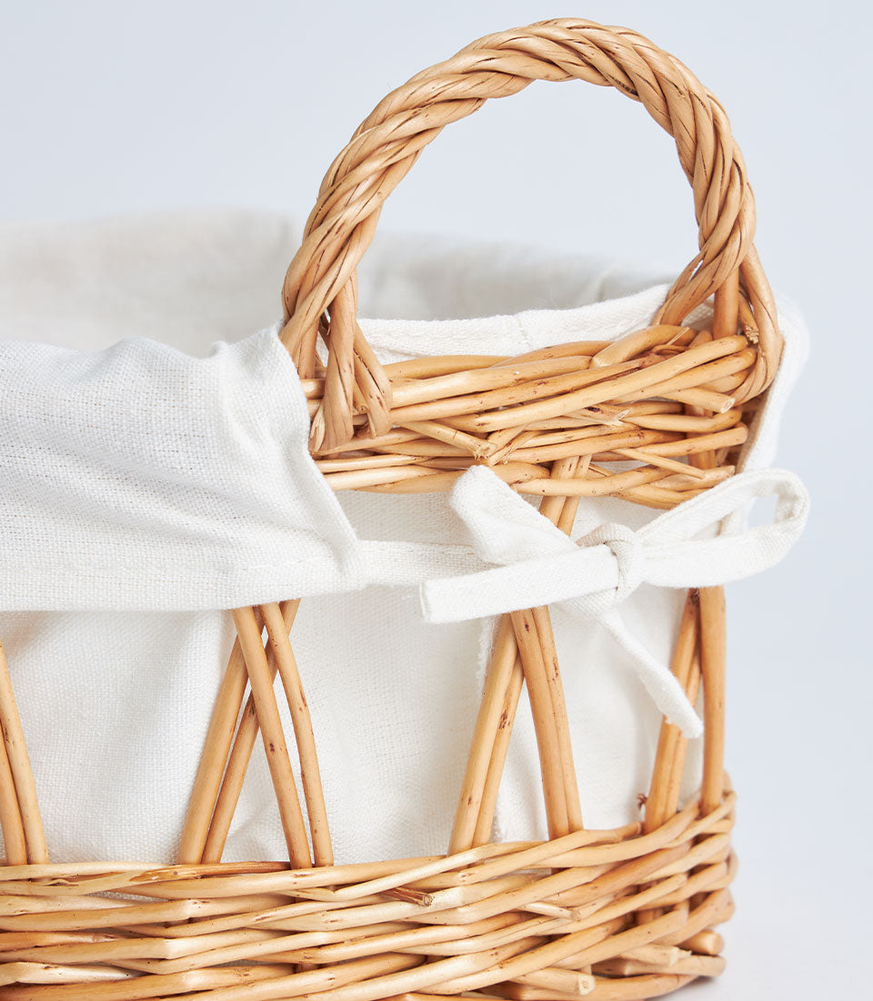 Light brown open weave wicker basket with white linen lining and braided handles