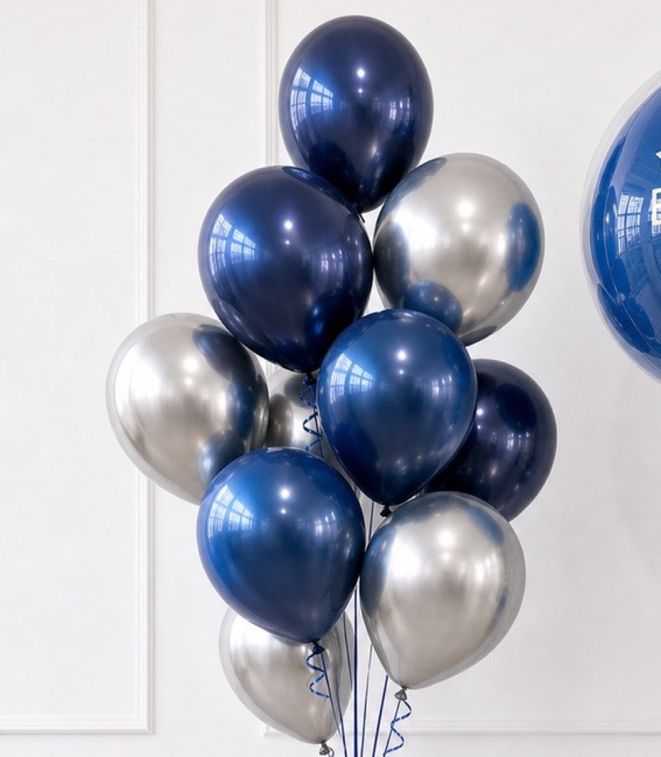 Metallic balloon bouquet with navy blue and silver chrome balloons arranged vertically with blue ribbons against a white wall.