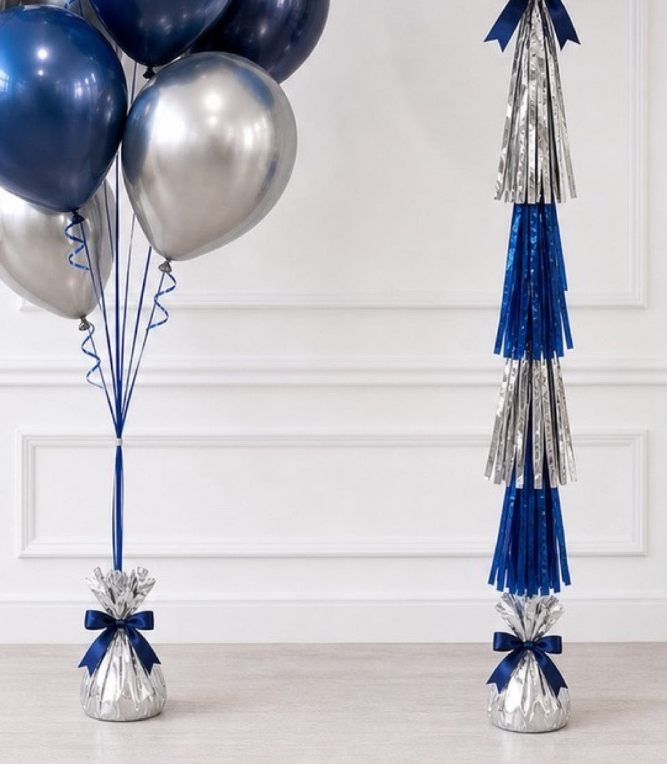Elegant blue and silver party decorations featuring metallic balloons, tassel garlands, and ribbon bows on white background.