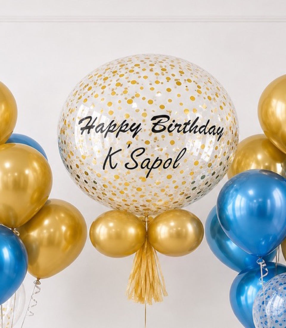 Large clear balloon with gold confetti and "Happy Birthday K'Sabol" text, surrounded by gold and blue metallic balloons with gold tassel.