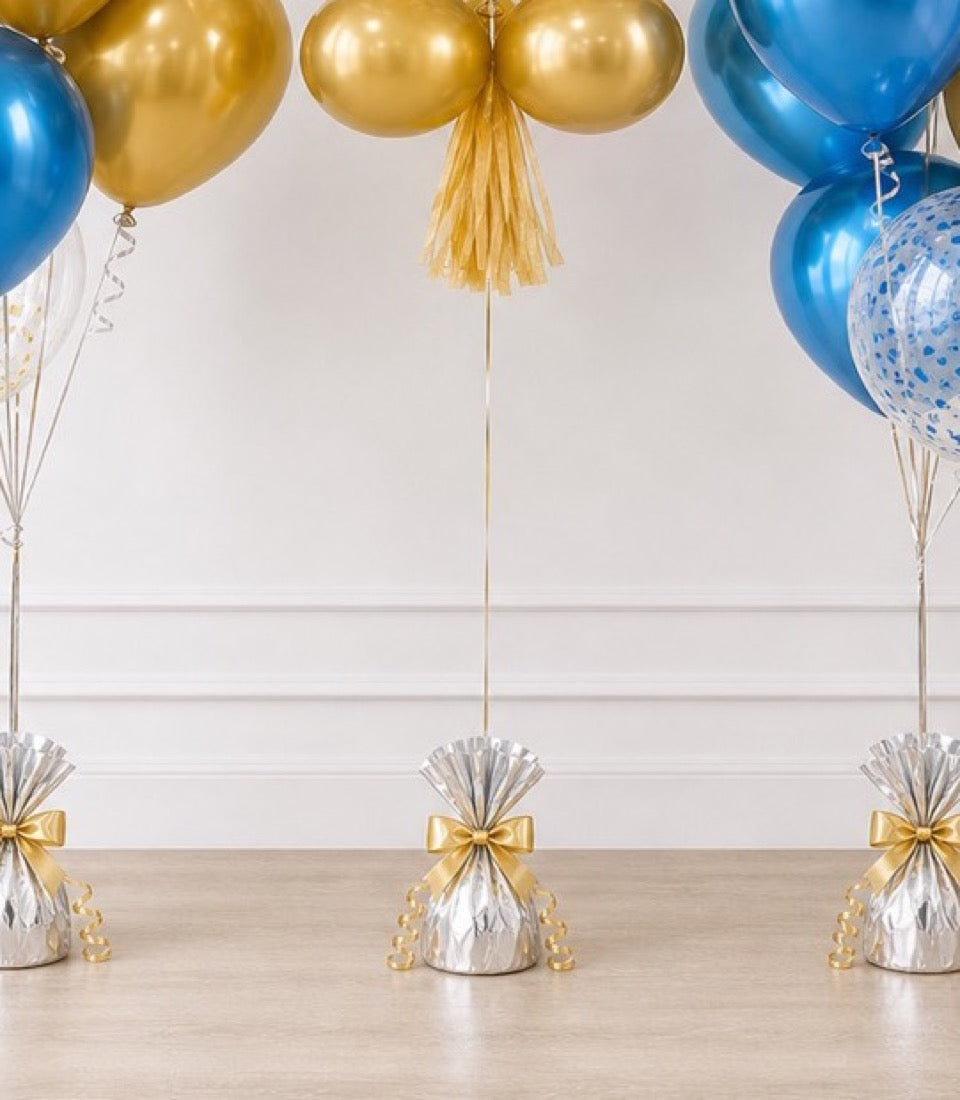 Elegant party balloons in gold and blue with metallic finishes, gold tassels, and silver foil balloon weights tied with gold bows on wooden floor.