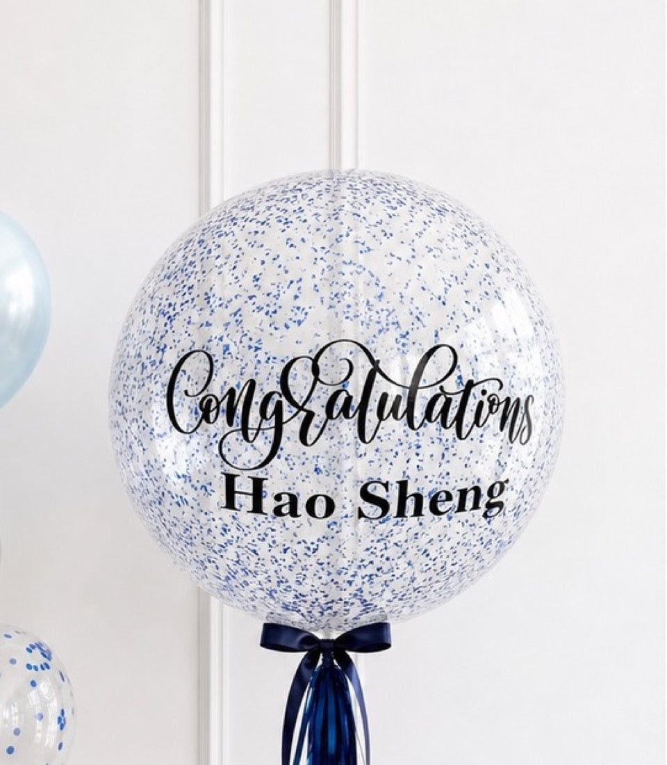 Large clear balloon filled with blue confetti, tied with navy ribbon bow, displaying "Congratulations Hao Sheng" text in elegant script.