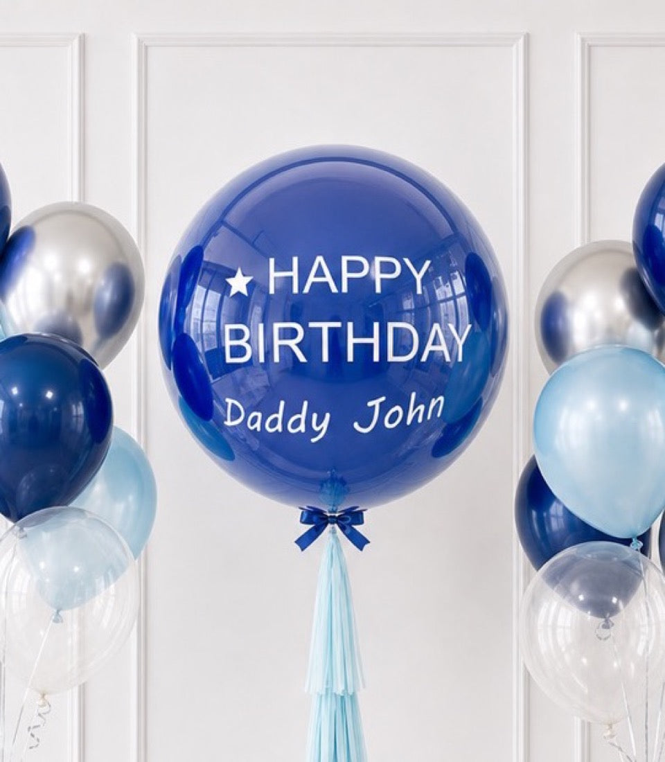 Blue bubble balloon with "Happy Birthday Daddy John" text, surrounded by silver and light blue balloons against white paneled wall.