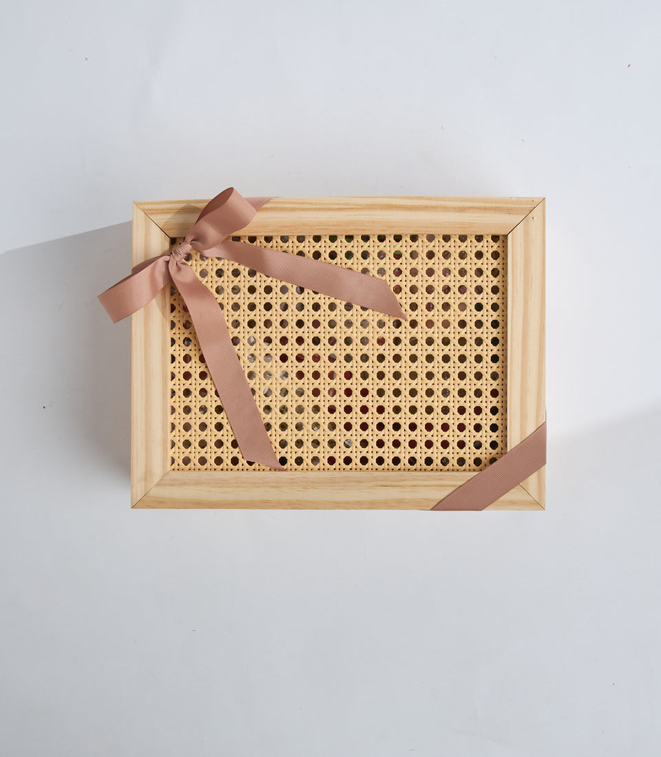 Wooden tray with woven rattan insert and mauve ribbon bow, displayed on white background in flat lay style.