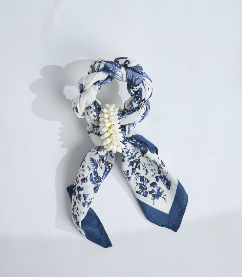 Blue and white floral print scarf with cream daisy flower embellishment, displayed in ribbon bow formation on white background.