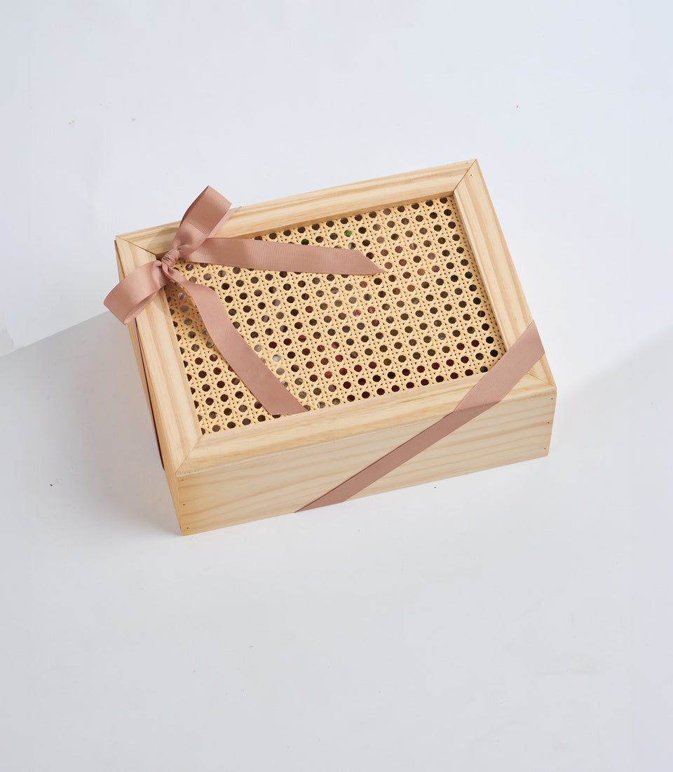 Wooden gift box with woven rattan panel and mauve ribbon bow on white background, minimalist packaging design.