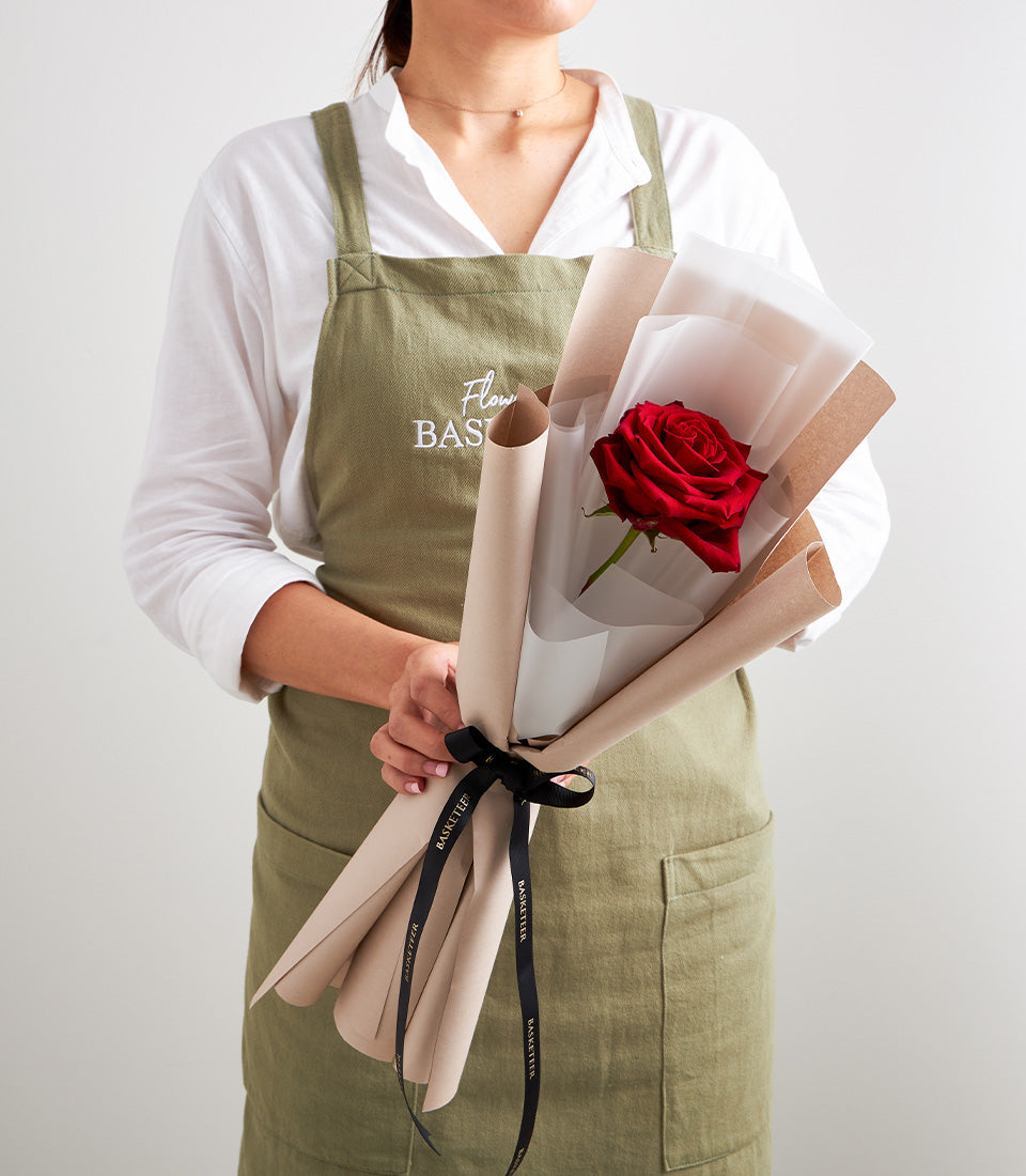 A single vibrant red rose, elegantly wrapped in premium beige paper and