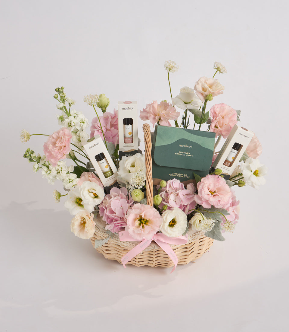 Luxury gift basket with pink and white carnations, white baby's breath flowers in woven basket, featuring Purebloom aromatherapy products and diffuser reeds with pink ribbon bow.
