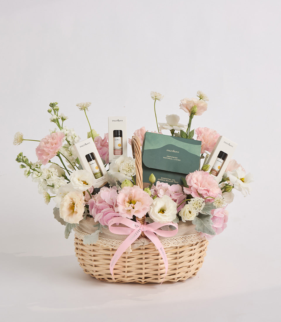 Luxe gift basket with pink and white carnations, cream wicker base, skincare products, green box, and pink ribbon bow on white background.