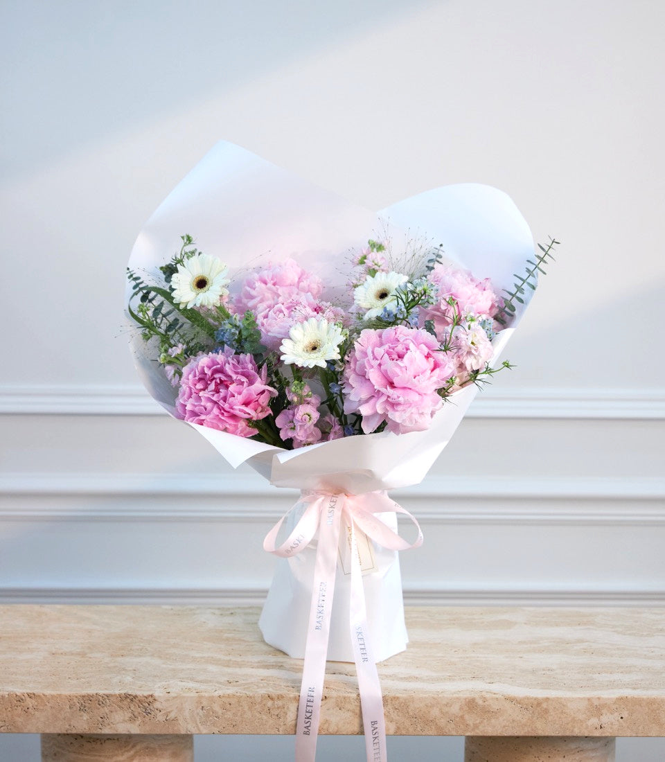 Elegant pink and white flower bouquet with peonies, gerberas, and eucalyptus wrapped in white paper with pink ribbon bow.
