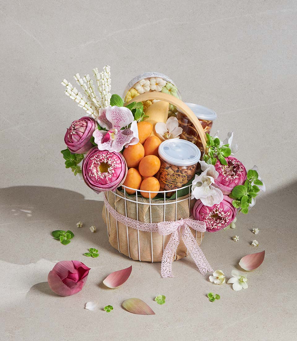 Luxury gift basket with fresh pink lotus blooms, orchids, dried fruits, and gourmet treats in white wire frame with burlap