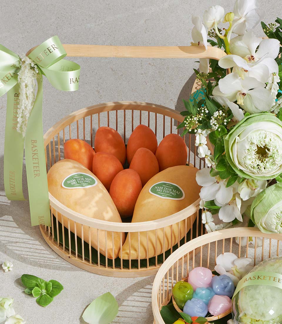 Songkran gift set with fresh Nam Dok Mai mangoes, orchids, lotus flowers, and pastel Thai desserts in wooden baskets