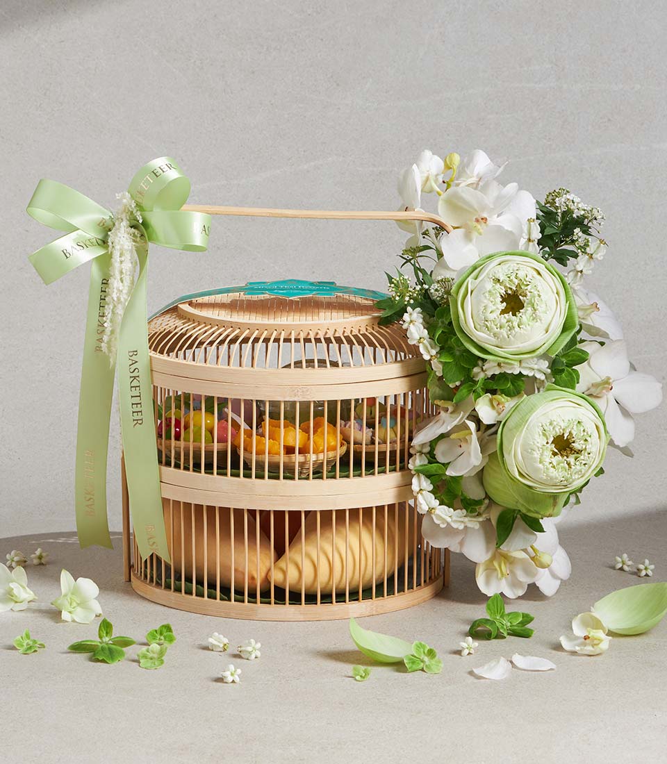 Bamboo birdcage gift basket with colorful sweets, pastries, white lotus flowers and orchids, green ribbon bow