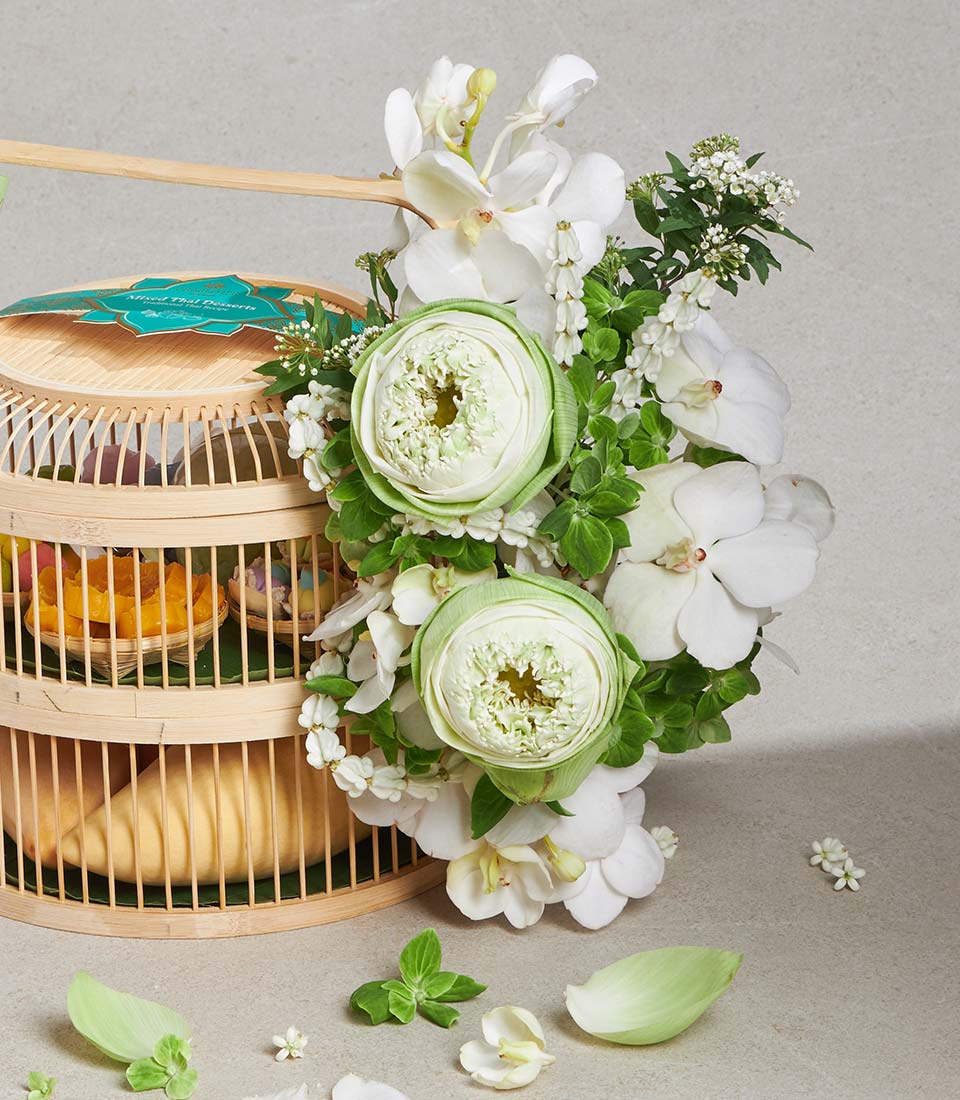 Bamboo birdcage gift set with white lotus and orchids, colorful Thai desserts in woven baskets, Songkran celebration gifting