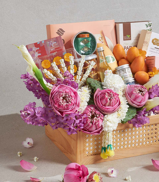 Light wood woven basket filled with gourmet treats, fresh mangoes, and vibrant pink lotus flowers with orchids and white
