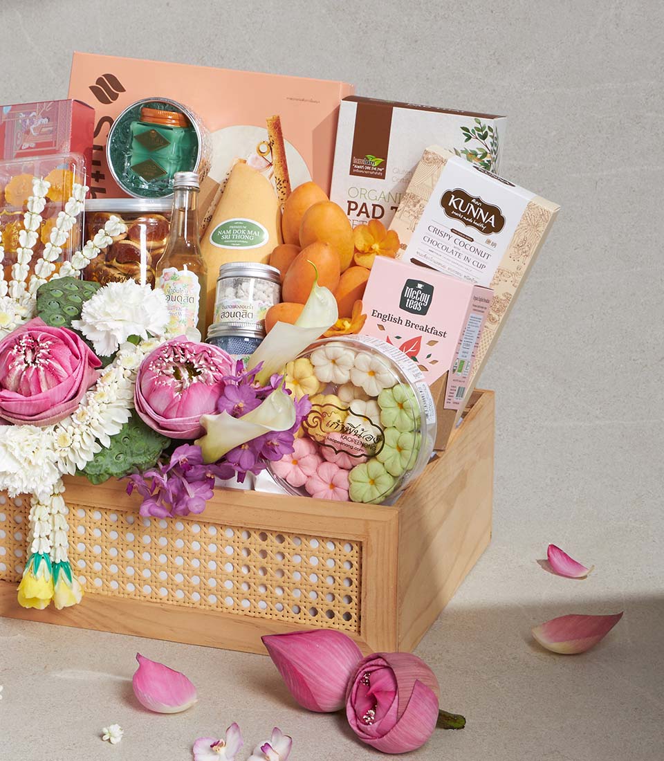 Wooden gift basket with Thai gourmet treats, flower-shaped cookies, and fresh pink lotus blossoms for Songkran gifting