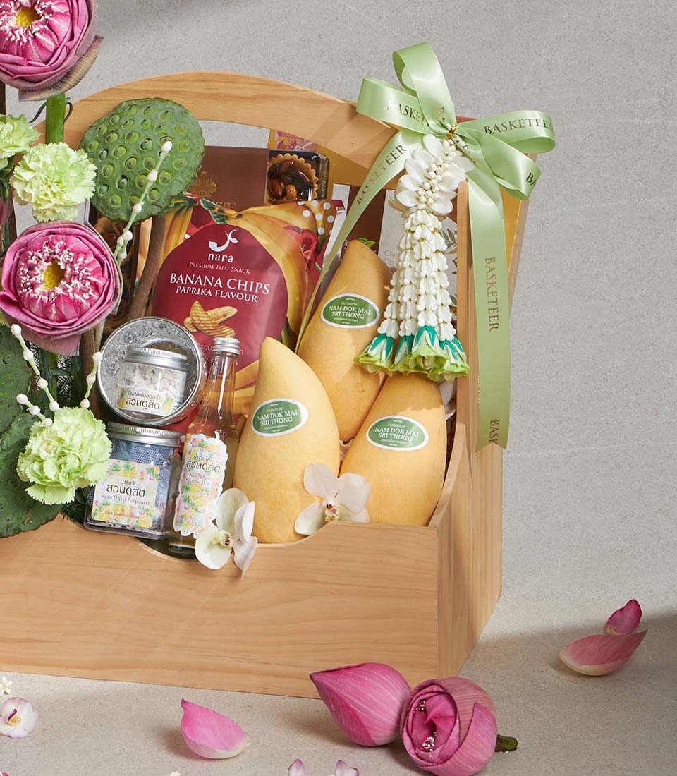 Wooden gift basket with Thai mangoes, banana chips, artisan preserves, fresh pink lotus flowers and green carnations for