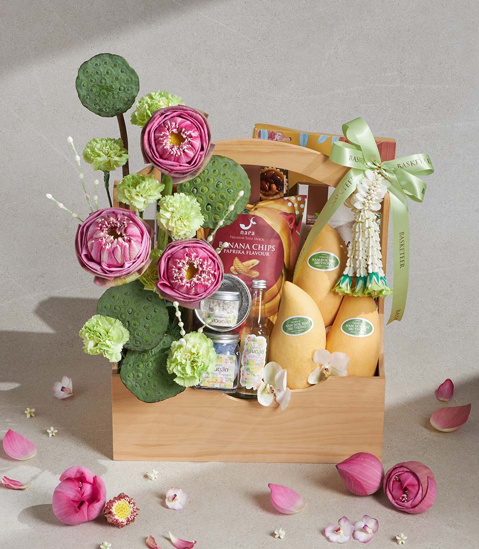Wooden gift basket with ripe mangoes, paprika banana chips, specialty jars, and pink lotus flowers for Songkran celebration