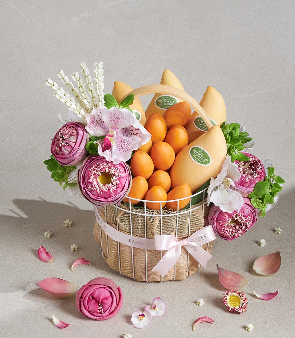 White wire gift basket with fresh mangoes, apricots, pink lotus flowers, orchids, and cascading petals